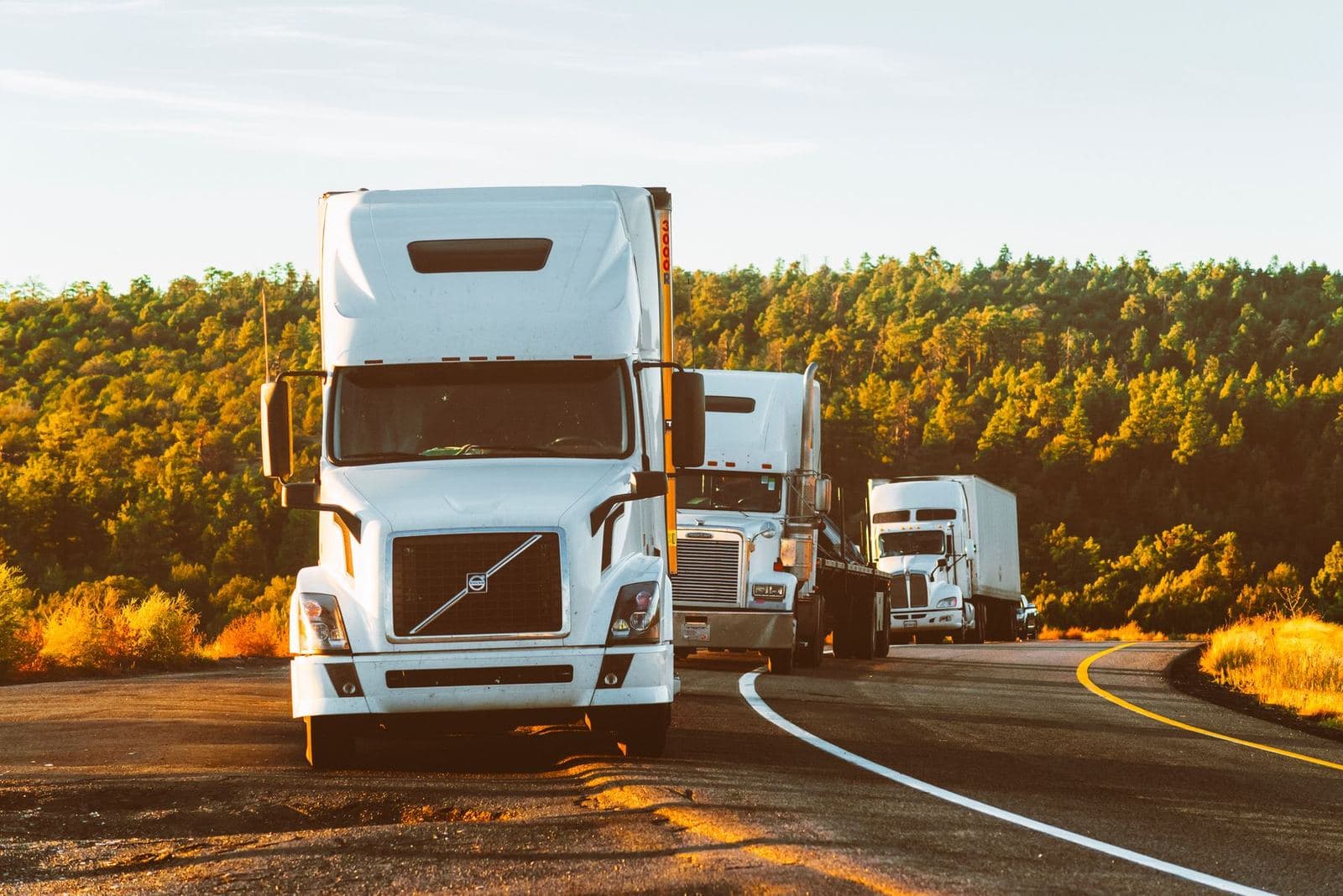 Three semi trucks on a highway at golden hour, the kind of small fleet Aditya Enterprises runs